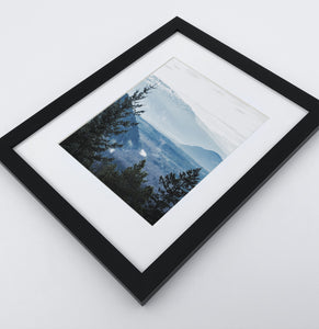 A photo print of blue mountains and a forest in black frame