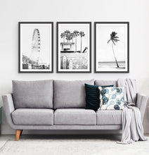 Load image into Gallery viewer, Photos of a ferris wheel, a boat coastal house with surfing boards and a palm on a beach, in frames hanging above the living room sofa
