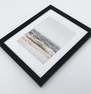 A photo print of sandy ocean shore in natural colors in a black frame