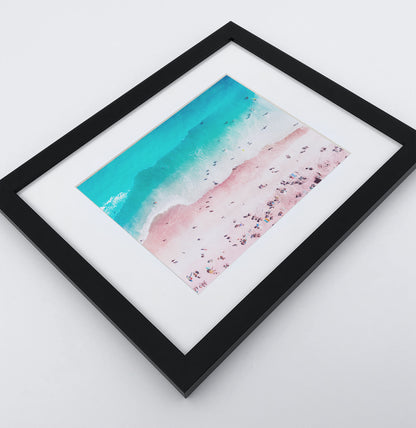 A bright azure and pink aerial photo print of a Californian coast in a black frame