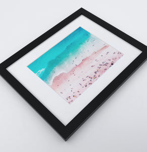 A bright azure and pink aerial photo print of a Californian coast in a black frame