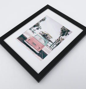 A bright pink aerial photo print of a surfing miniwan in a black frame