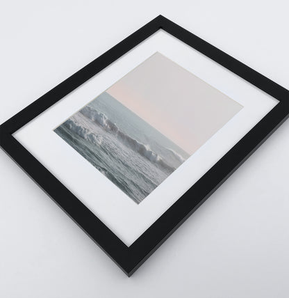 Big fluffy ocean waves in a light pink sunrise sky photo print in a black frame