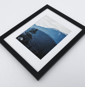 A photo print of blue mountains and a forest in black frame