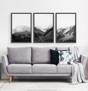 3 posters of black and white foggy mountain landscapes above a living room sofa