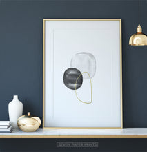Load image into Gallery viewer, A golden-framed wall art with black, silver and golden forms on a shelf
