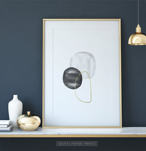 A golden-framed wall art with black, silver and golden forms on a shelf