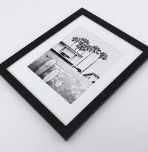 Load image into Gallery viewer, A boat coastal house with surfing boards in a black frame

