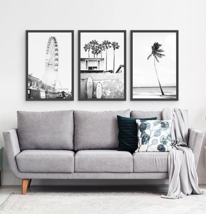 Photos of a ferris wheel, a boat coastal house with surfing boards and a palm on a beach, in frames hanging above the living room sofa