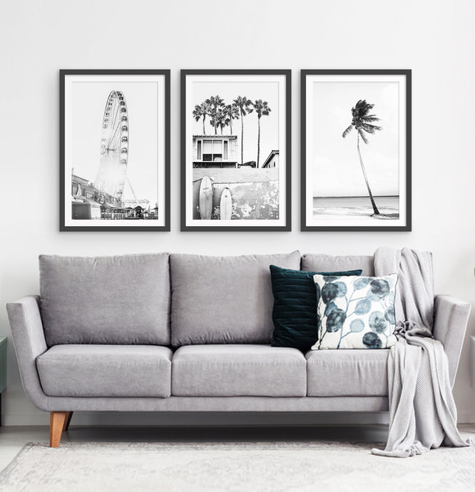 Photos of a ferris wheel, a boat coastal house with surfing boards and a palm on a beach, in frames hanging above the living room sofa