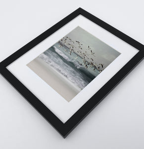 A framed print with seagulls flying above the ocean shore
